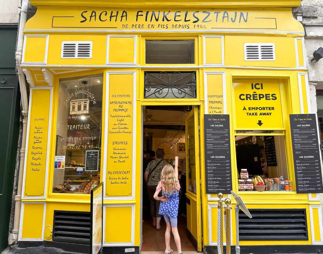 Child walking in the doorway of the yellow Jewish Sacha Finkelsztain deli in Paris